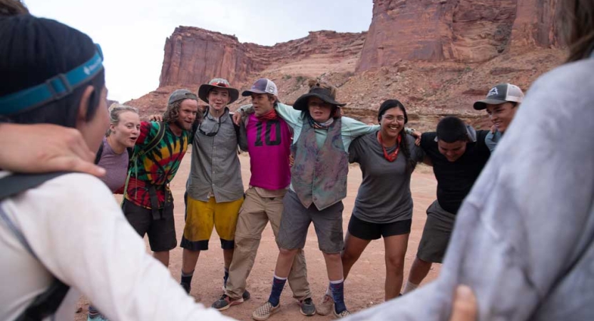 a group of people wrap their arms around each other in front of a vast red rock landscape